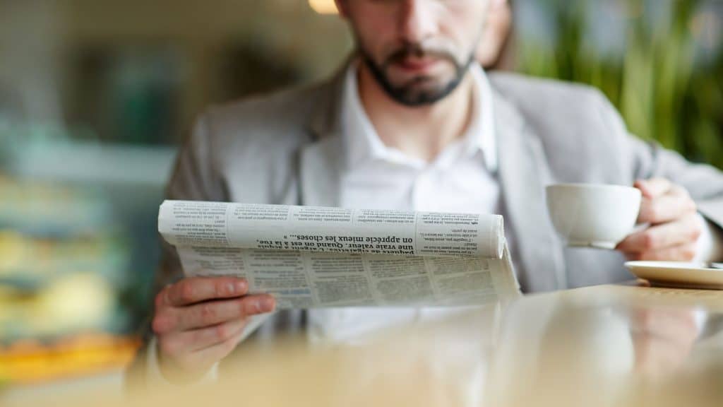 Man reading the newspaper with coffee in hand - GASB 75 makes it in the Wall Street Journal